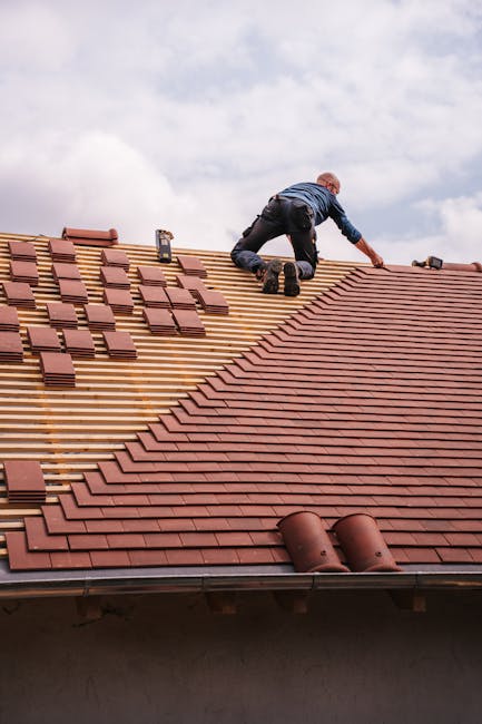 A roofer carefully installs shingles on a new residential roof under a cloudy sky.